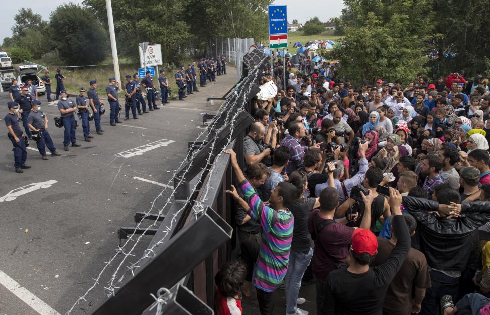Migrants stand in front of a barrier at the border with Hungary near the village of Horgos
